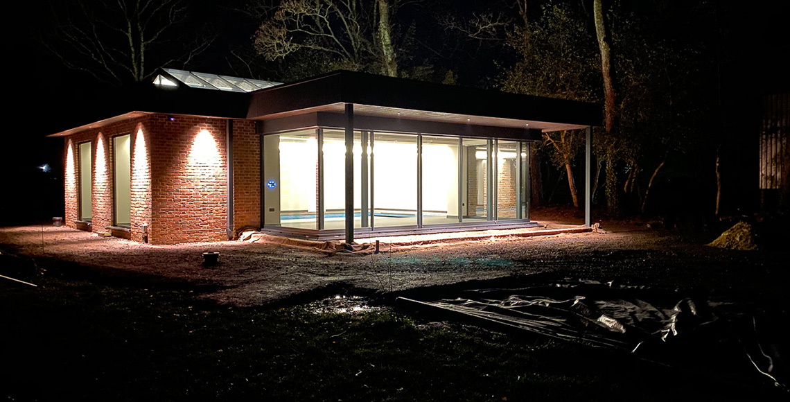 A night-time view of a gym building and pool under construction in the New Forest National Park area. A redesign and reconstruction project by INKSPACE Architects and Interior Designers